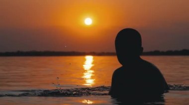 Gün batımı ve Turuncu Yol Arka Planda Suda Oturan Çocuk Silueti. Yavaş Çekim
