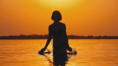 Gün batımında Kadın Siluet Ilerler Eller yükseltir ve Su Sıçramaları Oluşturma. Yavaş çekim