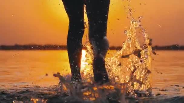 Silueta de piernas de niño corriendo hacia el agua al atardecer y creando salpicaduras. Moción lenta — Vídeos de Stock