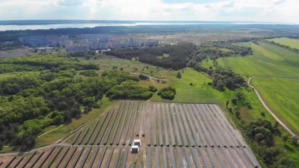 Widok z lotu ptaka na elektrownię słoneczną w zielonym polu niedaleko małego miasta w słoneczny dzień — Wideo stockowe
