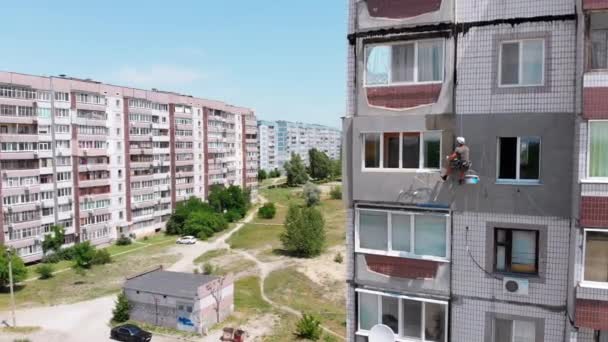 Вид с воздуха Промышленный альпинист Выполнение работ по изоляции бокового фасада здания — стоковое видео