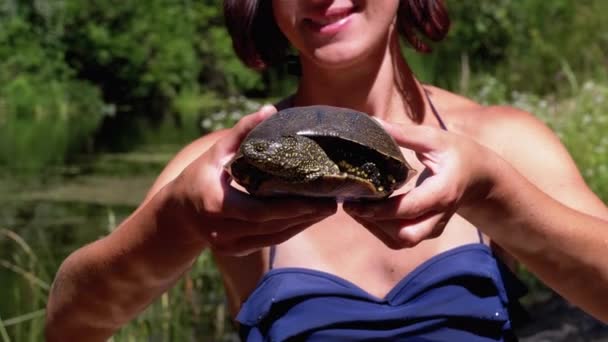 Mujer sostiene tortuga divertida en el brazo y sonríe en el río con vegetación verde — Vídeo de stock