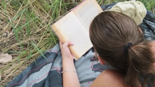 若い女性は夏の日に自然の中で草の上に横たわる本を読みます. — ストック動画
