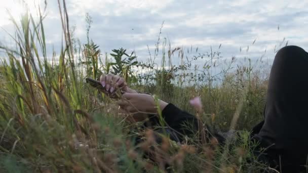 Jonge vrouw met behulp van smartphone liggen in het gras op de natuur in de lucht achtergrond — Stockvideo