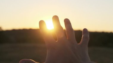 Erkek El Sunset 'e karşı. Güneşe dokun. Güneş parmaklarıyla parlar. Yavaş çekim