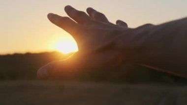 Erkek El Sunset 'e karşı. Güneşe dokun. Güneş parmaklarıyla parlar. Yavaş çekim