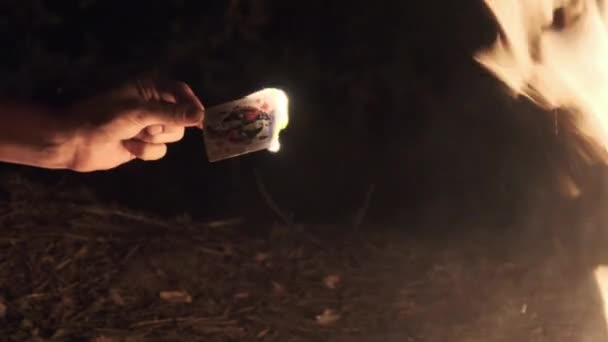 Main tient la carte brûlante sur fond noir près du feu de camp sur la nature. Mouvement lent — Video