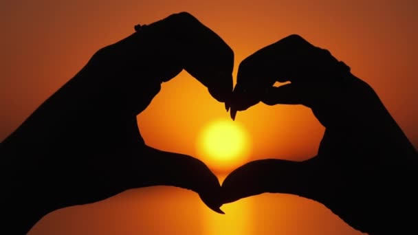 Silhouette weiblicher Hände mit Zeichen in Herzform bei orangefarbenem Sonnenuntergang — Stockvideo
