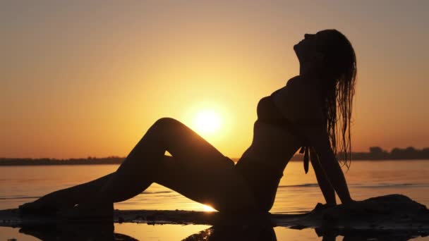 Silhouette di donna calda in costume da bagno sdraiata e in posa sulla spiaggia serale al tramonto — Video Stock