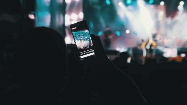 Mão masculina com smartphone fazendo transmissão ao vivo em redes sociais no concerto. Movimento lento — Vídeo de Stock