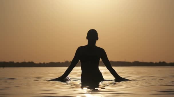 Silhouette de la jeune femme joyeuse éclaboussant l'eau de la rivière au coucher du soleil. Mouvement lent — Video