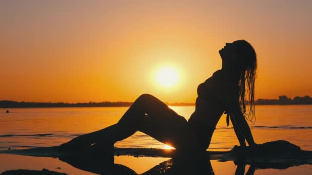 水着で熱い女のシルエットが横たわると日没で夕景のビーチでポーズ — ストック動画