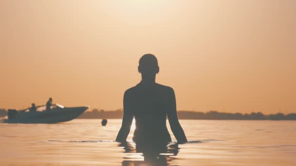 Silhouet van de jonge vrolijke vrouw die bij zonsondergang rivierwater spettert. Langzame beweging — Stockvideo
