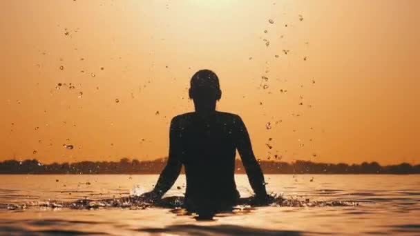 Silhouette della giovane allegra donna allegra che spruzza l'acqua del fiume al tramonto — Video Stock