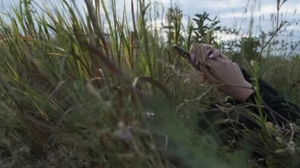 젊은 여자가 스마트폰을 사용하여 공중 배경에서 자연의 풀밭에 누워 있는 모습 — 비디오