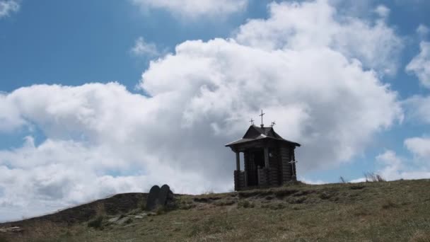 Mała drewniana kaplica na szczycie góry na tle ruchomych chmur na niebie. — Wideo stockowe