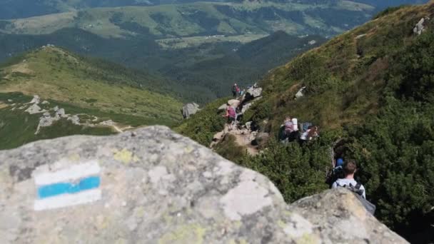 Ομάδα τουριστών και παιδιών με σακίδια κατεβαίνουν στο πέτρινο μονοπάτι στο βουνό — Αρχείο Βίντεο