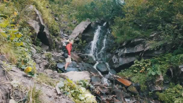 Tourist mit Rucksack kam zum Bergwasserfall und breitete Arme zur Seite aus — Stockvideo