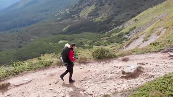 バックパック付きの旅行者写真家の空中ビュー山脈によるクライミング — ストック動画