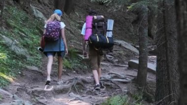 Sırt çantalı bir çift turist dağ ormanındaki taş patikaya tırmanıyor.
