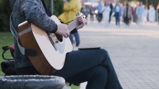 Jovem músico de rua tocando guitarra acústica no parque. As pessoas passam — Vídeo de Stock