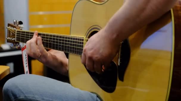 Gitarrist oder Verkäufer in einem Musikladen, der eine Akustikgitarre mit Preisschild spielt — Stockvideo