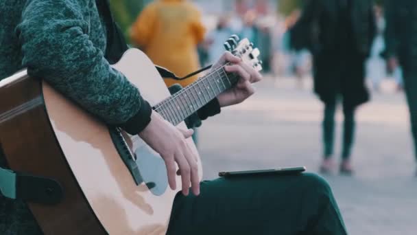 Молодой уличный музыкант играет на акустической гитаре в парке. Люди идут мимо — стоковое видео