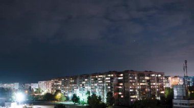 Yıldızlar ve Gece Bulutları çok katlı binaların üzerinden geçiyor. Gece şehri. Zaman Uygulaması.