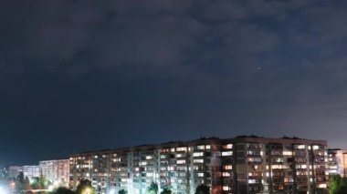 Yıldızlar ve Gece Bulutları çok katlı binaların üzerinden geçiyor. Gece şehri. Zaman Uygulaması.