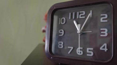 Bir komodinin üzerinde antika bir kahverengi kare çalar saat gösterilir. Beyaz ikinci eli sürekli hareket ediyor. Bu da arka planda oyuncaklar olan sessiz bir yatak odasında zamanın akışını gösteriyor..