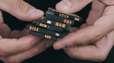 Cep telefonlarından alınmış eski, kullanılmış lityum iyonlu pilleri tutarken ve çevirirken yakın plan çekimler. Siyah zemin ile elektronik atık ve geri dönüşüm kavramı.