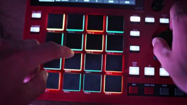 El kameraları dinamik bir şekilde ışıklandırılmış pedleri çalıyor ve kırmızı dijital bir dayakçının düğmesini ayarlıyor, yer değiştiren ışıklarla bir stüdyo ortamında canlı müzik yaratıyor..