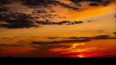 Güneş siluetli bir ufkun altına batarken, zaman çizelgesi çarpıcı bir günbatımını yakalıyor. Gökyüzünde dramatik turuncu ve kırmızı bulutlar sürükleniyor, alacakaranlıktan alacakaranlığa manzaralı bir manzarayla geçiş yapıyorlar..