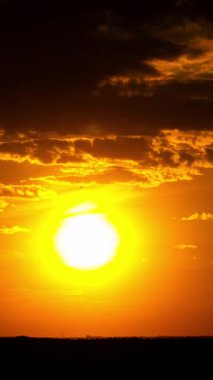 Dikey zaman çizelgesi, parlak bir güneşin parlak bir altın gökyüzüne doğru battığını gösteriyor. Karanlık bulutlar sahnenin üstünü çerçeveler, altta koyu siluetli bir manzara, sosyal medya için mükemmel..