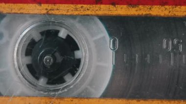 Eski bir teyp içinde çizilmiş plastik, aşınmış doku ve sayısal sayaç işaretlerini gösteren grungy ses kaseti üzerinde dönen tek bir makaranın aşırı yakın çekim makro görüntüsü..