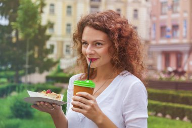 Parkta güzel bir kız bir saman kağıt bardak dan bir fincan kahve içer ve lezzetli elma pie.the kız içecekler kahve payet aracılığıyla tutar