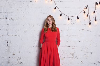 Studio fotoğraf makinesi üzerinde tuğla duvar arka plan önünde poz kırmızı elbiseli Genç güzel kız. Farklı insan duygu, beden dili.