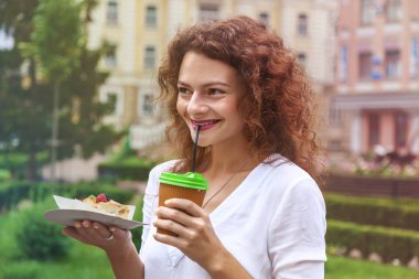 Parkta güzel bir kız bir saman kağıt bardak dan bir fincan kahve içer ve lezzetli elma pie.the kız içecekler kahve payet aracılığıyla tutar