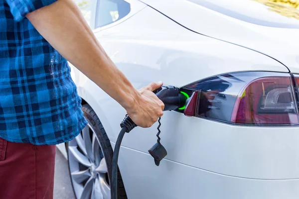 Man inserts the charger into an electric vehicle. Electric vehicle charging station for home with EV car background
