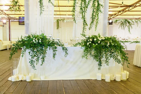 Design and decor decoration of the wedding celebration with white roses, green leaves, candles and bouquets of flowers