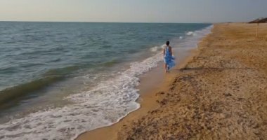 Güzel genç kız sahilde denizin mavi elbiseli bir kenarında ayakta. Sahilde denize yakın bir elbise kız.