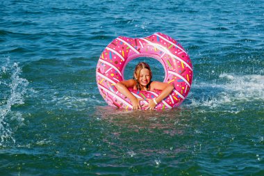 Bir kız çörek şeklinde şişme bir daire ile denizde yüzme. Denizde aile tatili