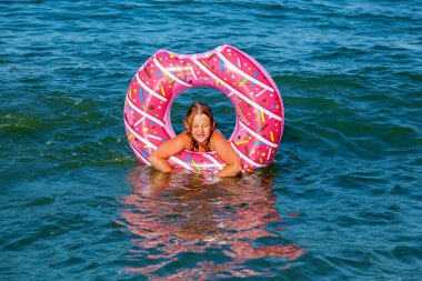 Bir kız çörek şeklinde şişme bir daire ile denizde yüzme. Denizde aile tatili