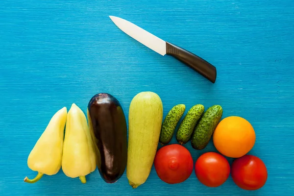 Vegetables are whole and cut a notepad for writing ricepts and a ceramic knife on a blue board.