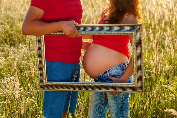 Chica embarazada en la naturaleza en jint y camiseta roja en un campo al atardecer —  Fotos de Stock