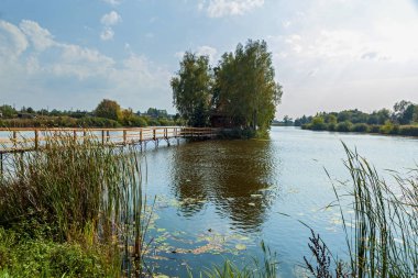 Adadaki küçük ev. Göl kenarındaki eve giden köprü manzarası. Adadaki eski ahşap balıkçı ve avcı evi. Eski Solotvyn Köyü, Ukrayna