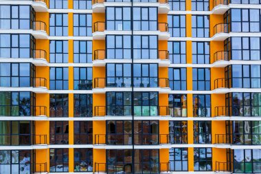 Yüksek katlı bir binadaki apartmanların cam ön cephesi. Modern bir binanın tasarımında pencere ve balkonlar.