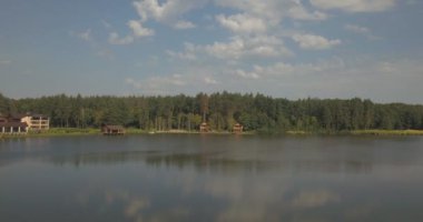 Göl kenarındaki ahşap ev ve temiz su. Gölet, sık yeşil ormanı ve beyaz derili gökyüzünü yansıtır. Gölde küçük, rahat bir ev. Güzel manzara.