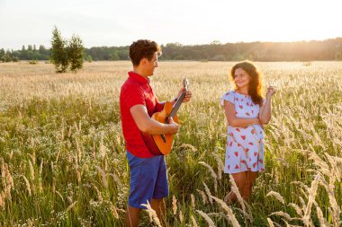 Gitarlı genç bir adam güneşli bir günde hamile karısının yanında duruyor..