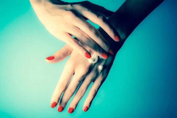 Hands of a young girl with red nails and drops of cream close-up on a blue background. Vintage, grunge old retro style photo.